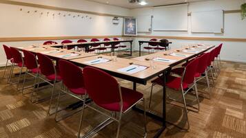 Un salón de conferencias con varias mesas, sillas rojas y una pizarra.