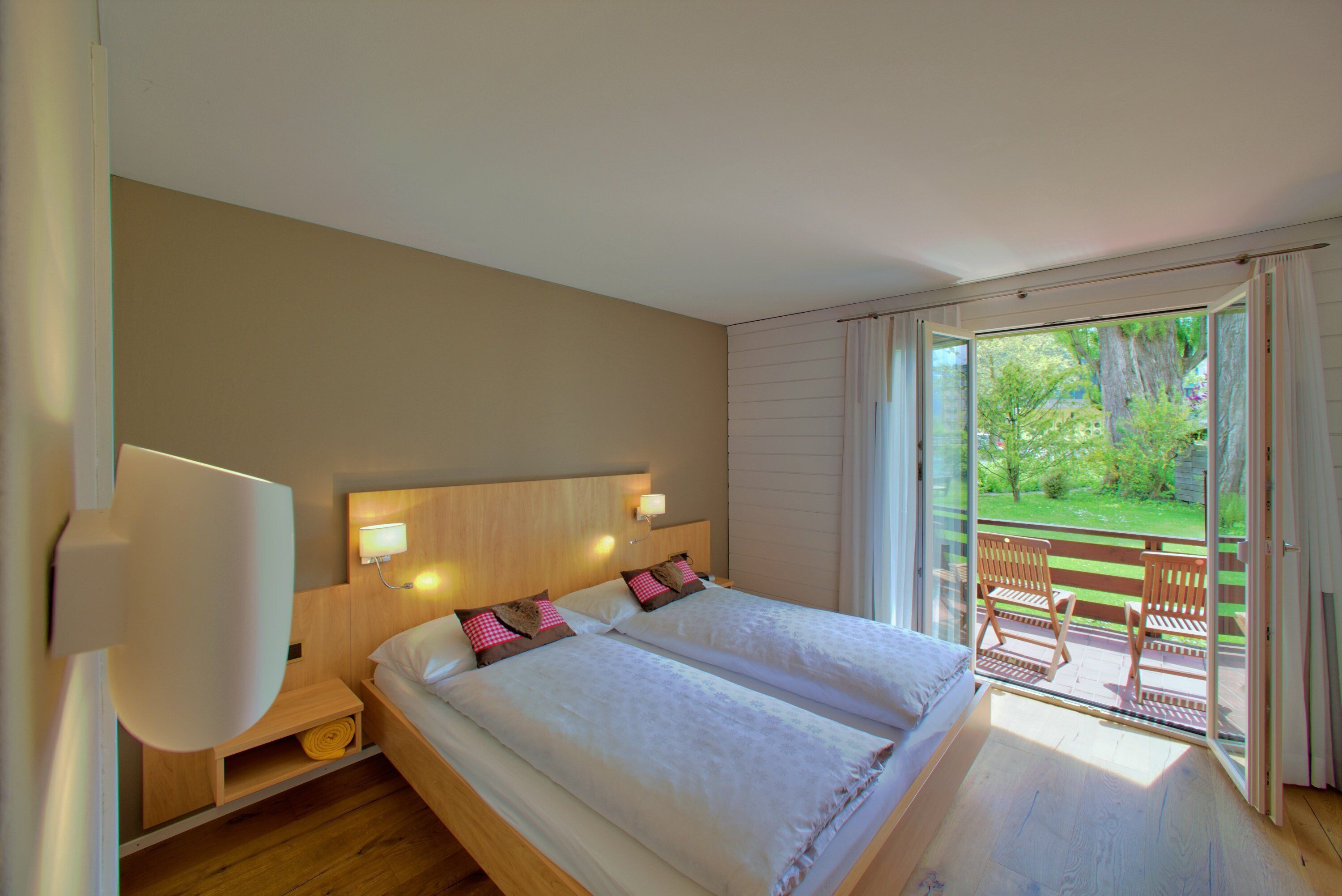 Un dormitorio con dos camas, cabeceros de madera, una mesita de noche y vistas a un balcón con sillas.