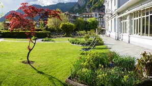 A well-maintained garden with a red-leafed tree, a lawn, and a building with large windows and a balcony. - Boutique Hotel Bellevue (Interlaken)