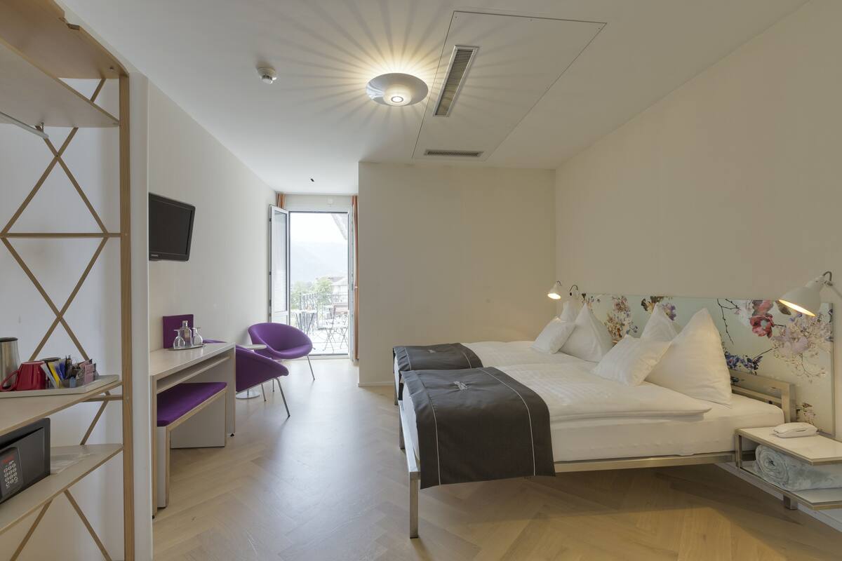 A modern hotel room with a bed, a desk, a chair, and a TV.