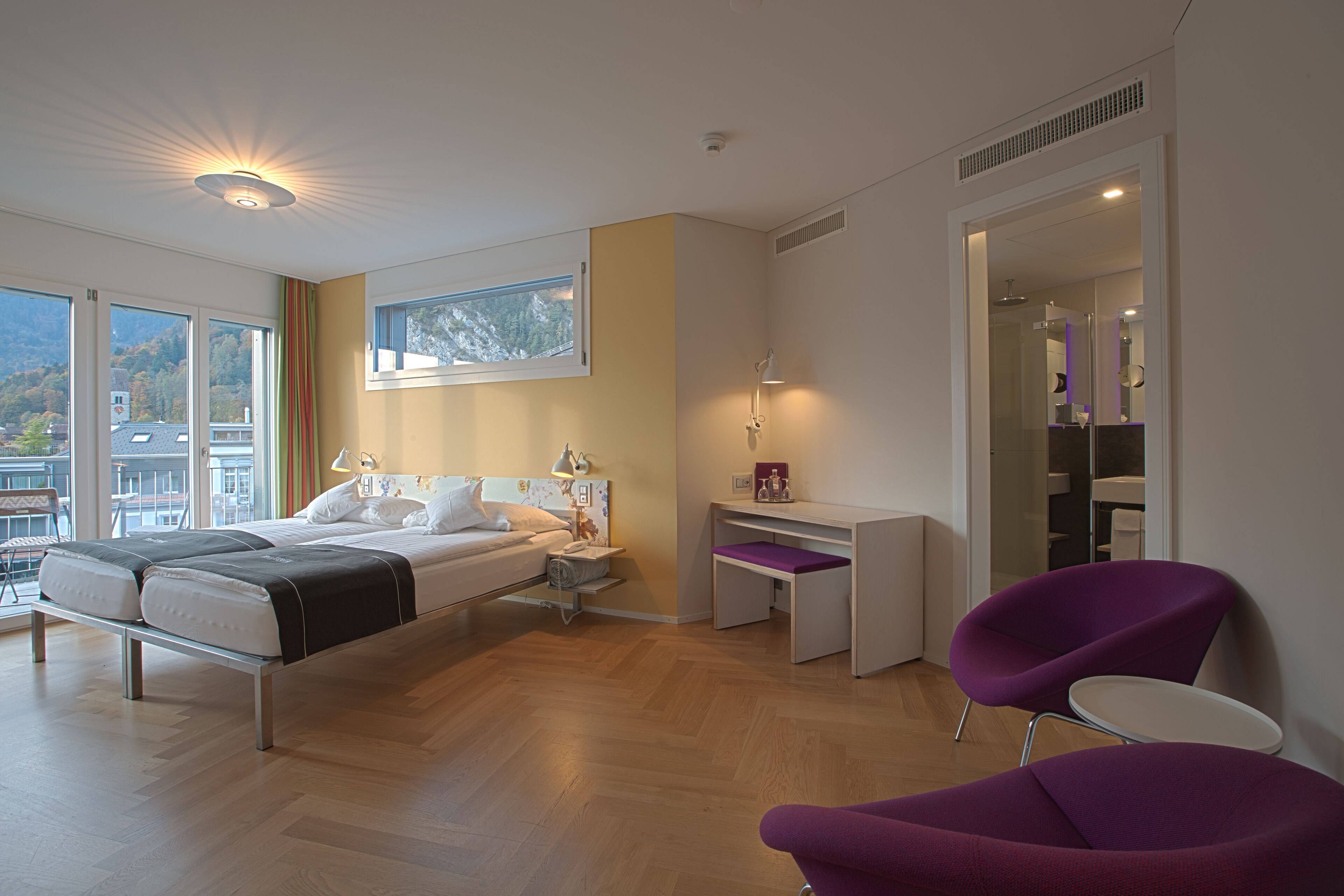 A modern bedroom with a bed, bedside table, and a desk with a chair.