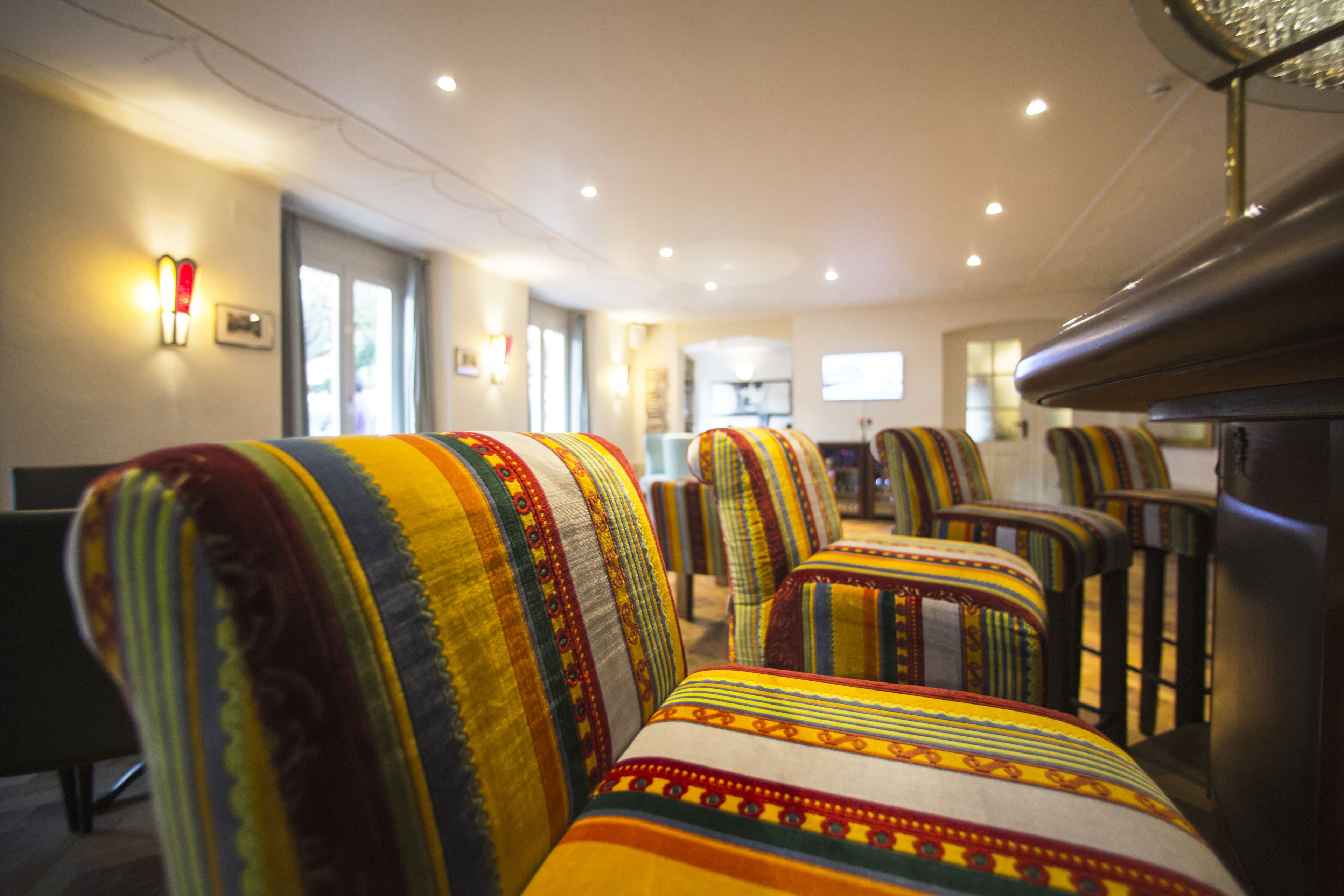 Une rangée de fauteuils aux couleurs vives et aux motifs variés se trouve dans une pièce bien éclairée, dotée d’un plafond moderne et d’un téléviseur en arrière-plan.