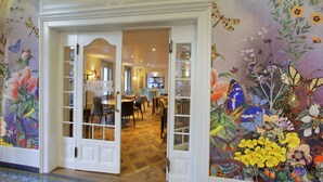 A hotel lobby with a floral mural, a reception desk, and a dining area with chairs and tables. - Boutique Hotel Bellevue (Interlaken)