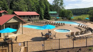 A pool area with lounge chairs and umbrellas, surrounded by a wooden deck and a fenced pool. - Mountain Lake Lodge (Pembroke)