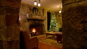 A stone fireplace with a lit fire, a Christmas tree, and a cozy seating area with a chair and a table. - Mountain Lake Lodge (Pembroke)