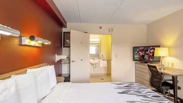 Ein Hotelzimmer mit Bett, Schreibtisch, Sessel, Fernseher und einem durch eine offene Tür einsehbaren Badezimmer.