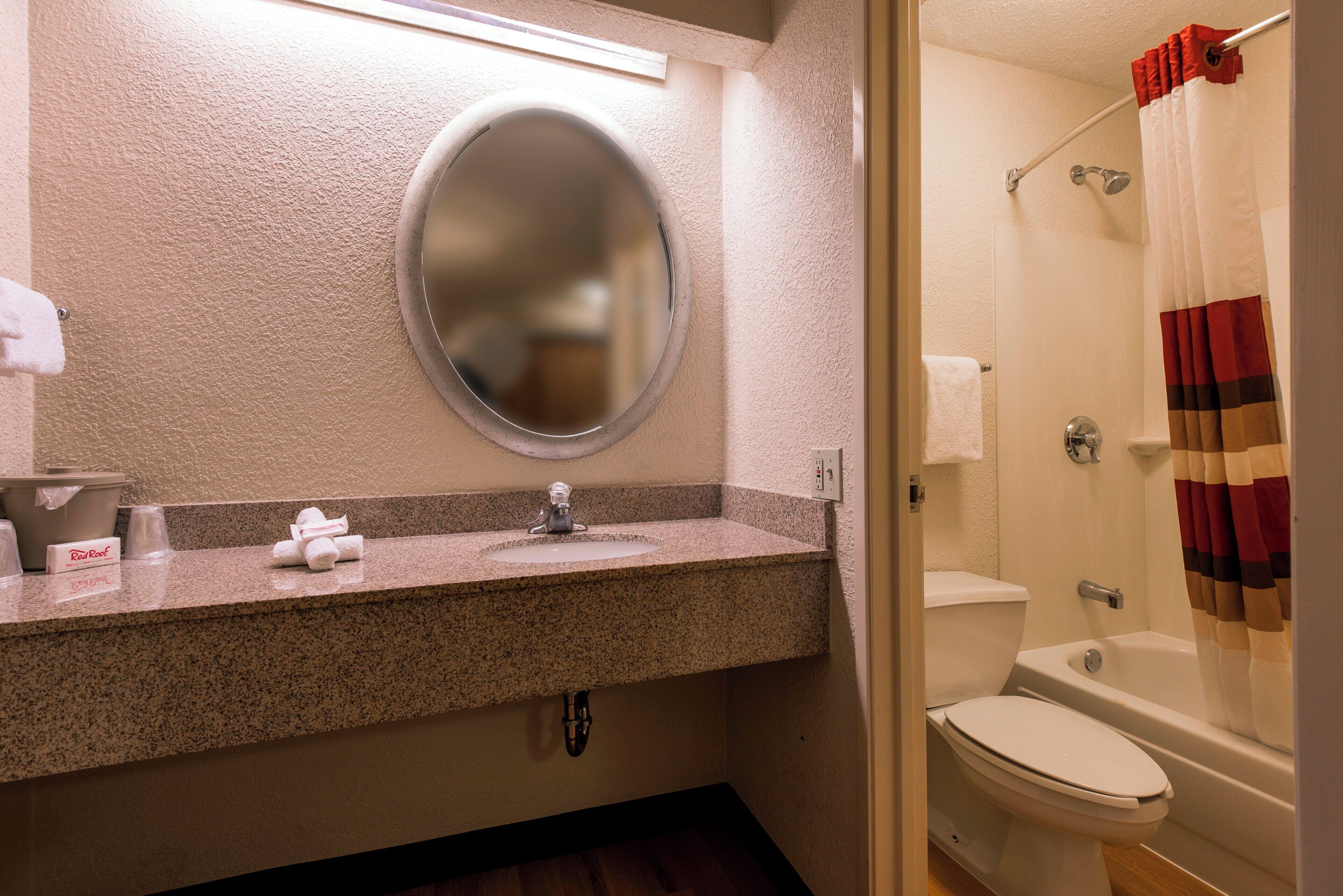A bathroom with a granite countertop, a round mirror, a toilet, and a shower curtain.