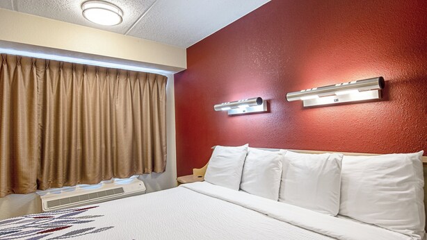 A hotel room with a bed, curtains, a wall-mounted air conditioning unit, and a wall-mounted light fixture. - Red Roof Inn Fairmont (Fairmont)