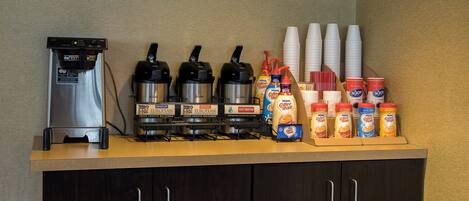 A coffee station with a coffee machine, multiple coffee dispensers, disposable cups, and a variety of coffee creamer options.