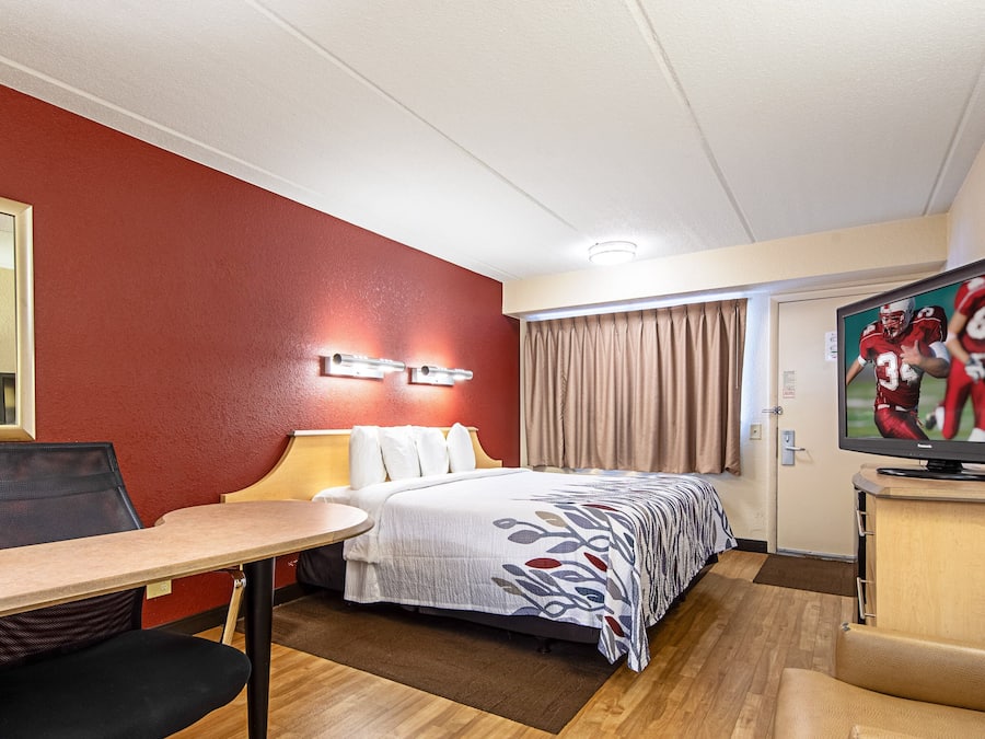 Una habitación de hotel con una cama, un escritorio, una silla, un televisor y una puerta.