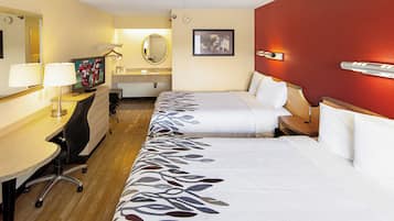 Een hotelkamer met twee bedden, een bureau, een stoel, een televisie, een spiegel, een wastafel en een rode accentmuur.
