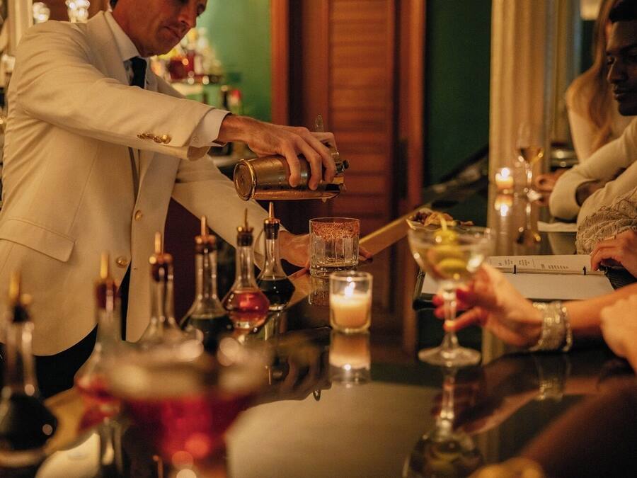 A bar setting with a bartender preparing a drink, a candle on the table, and a menu.