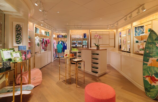 Interior de un hotel boutique con pisos de madera, un mostrador de recepción, un área de descanso y una exhibición de ropa.