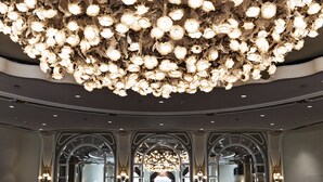 A grand chandelier with multiple tiers of lights, arched doorways, and a reflective ceiling.