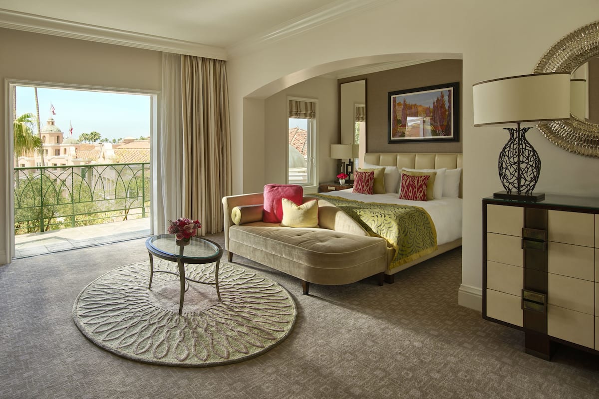 Ein Hotelzimmer mit einem Bett, einem Sofa, einem runden Teppich, einem Schreibtisch und Blick auf ein Gebäude.