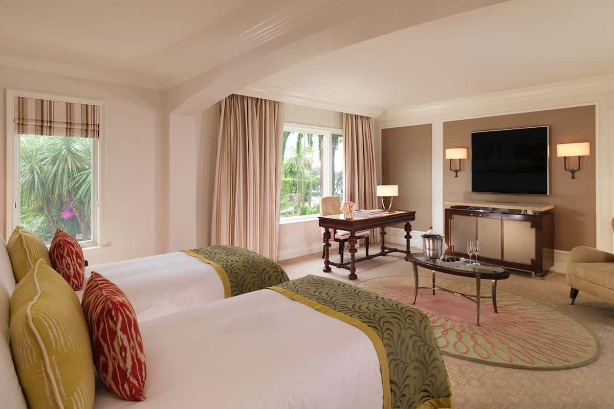 Ein Hotelzimmer mit zwei Betten, einem Schreibtisch, einem Sessel und Blick auf Grünflächen.