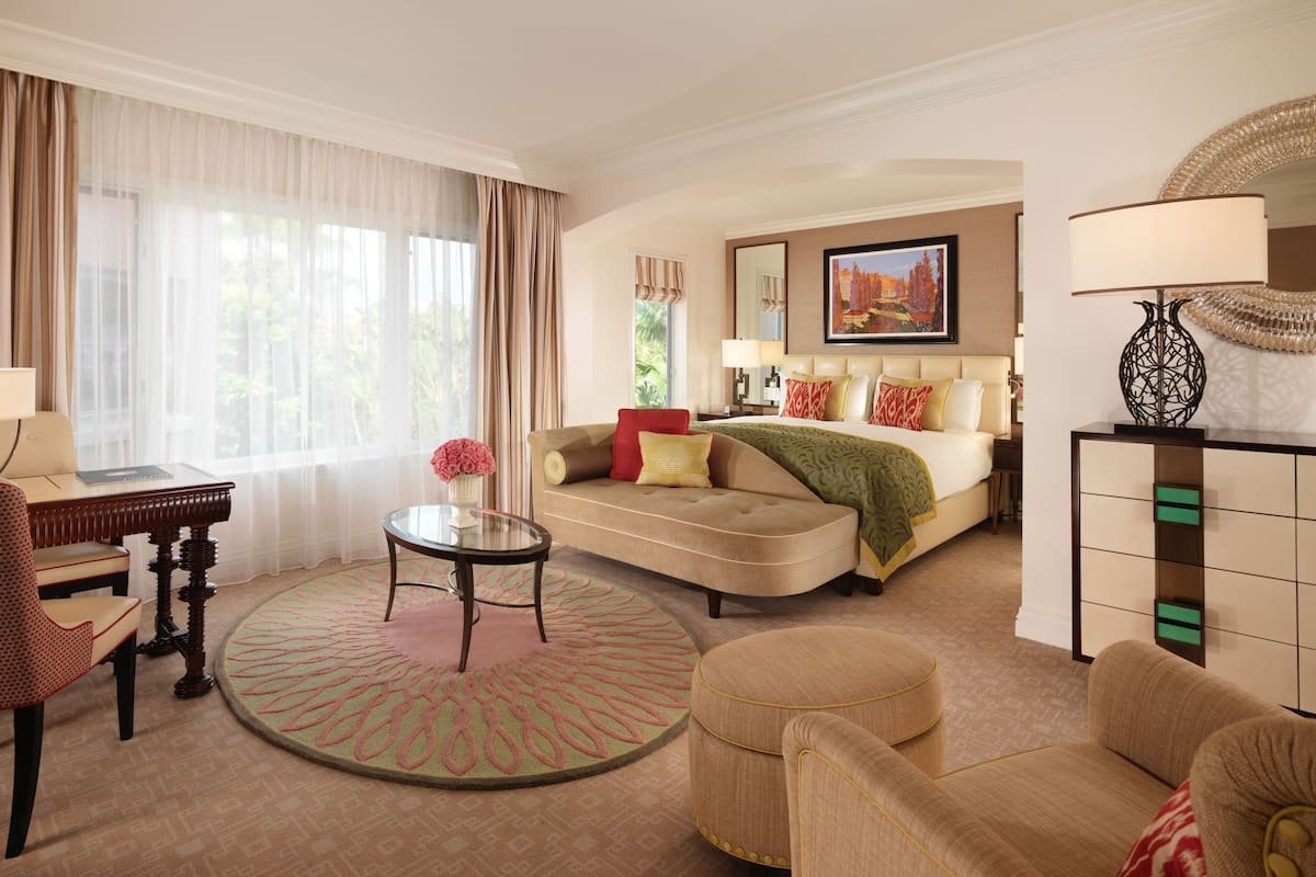Ein Hotelzimmer mit Sofa, Sessel, rundem Tisch und einem Bett mit grüner Tagesdecke.