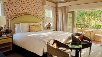Une chambre d’hôtel avec un grand lit, deux chaises, une petite table et un balcon donnant sur la forêt.