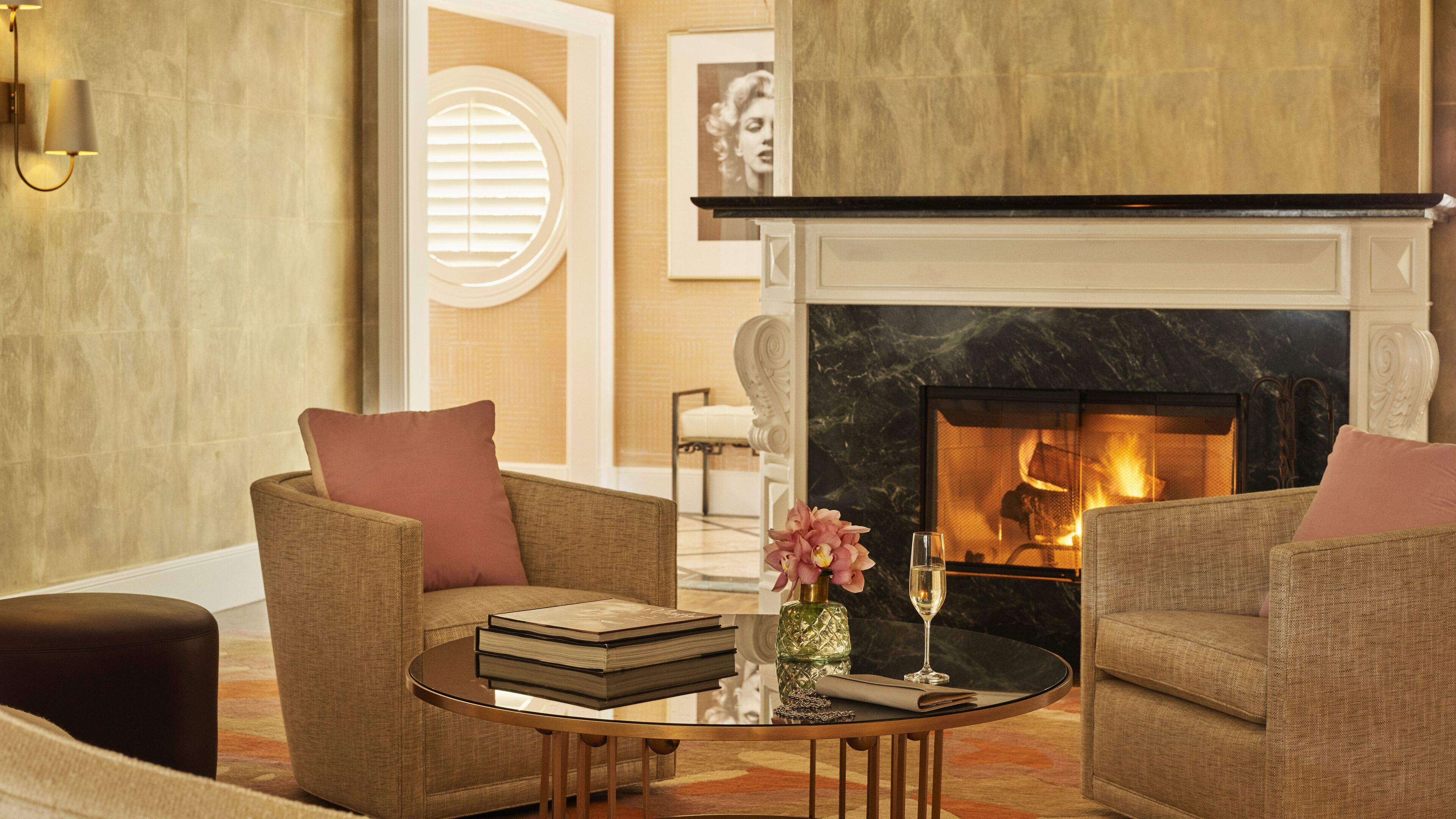 Un salon chaleureux avec deux fauteuils, une table basse ornée de livres et d’un vase de fleurs, une cheminée et un portrait encadré accroché au mur.