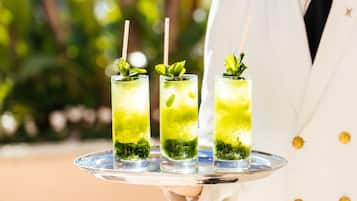 A person holding a tray with three glasses of green beverage, each garnished with mint leaves and straws.