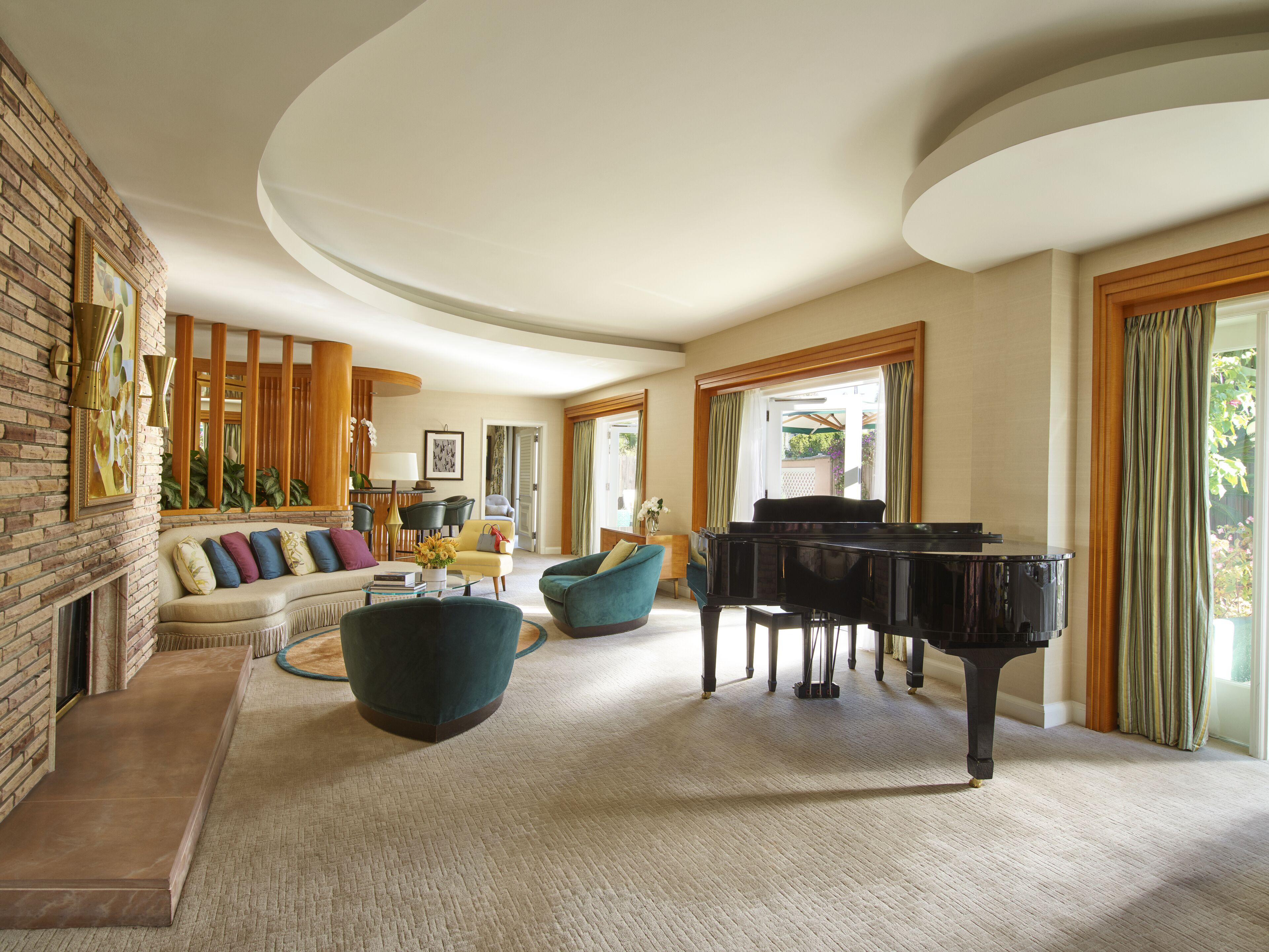 A spacious living room with a grand piano, comfortable seating, a fireplace, and large windows offering natural light.