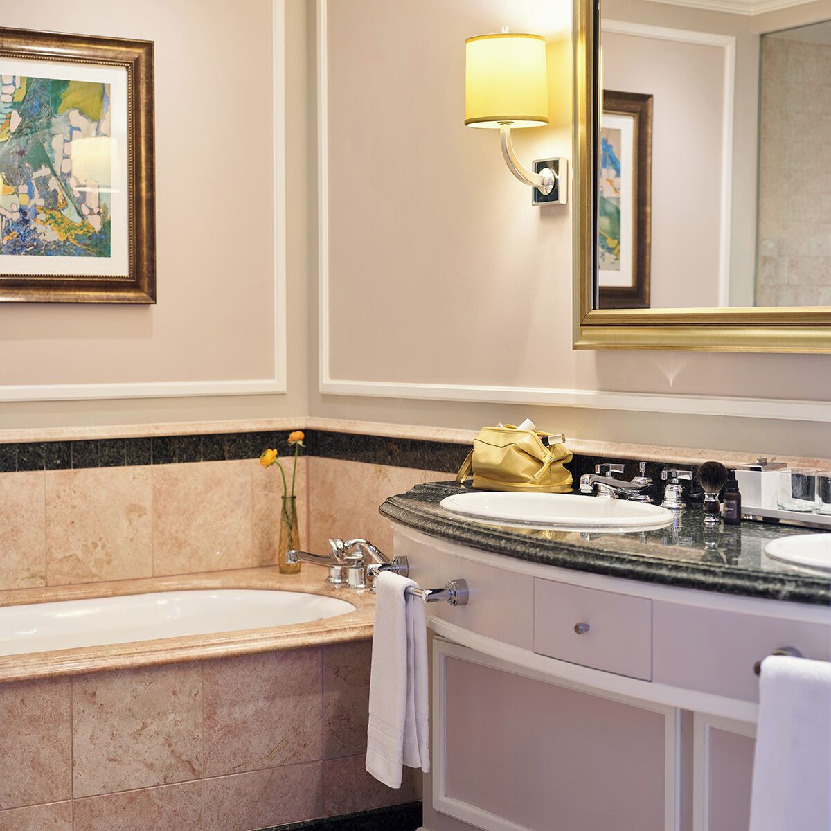 A bathroom with a bathtub, two sinks, a vanity, a mirror, and a framed painting on the wall.