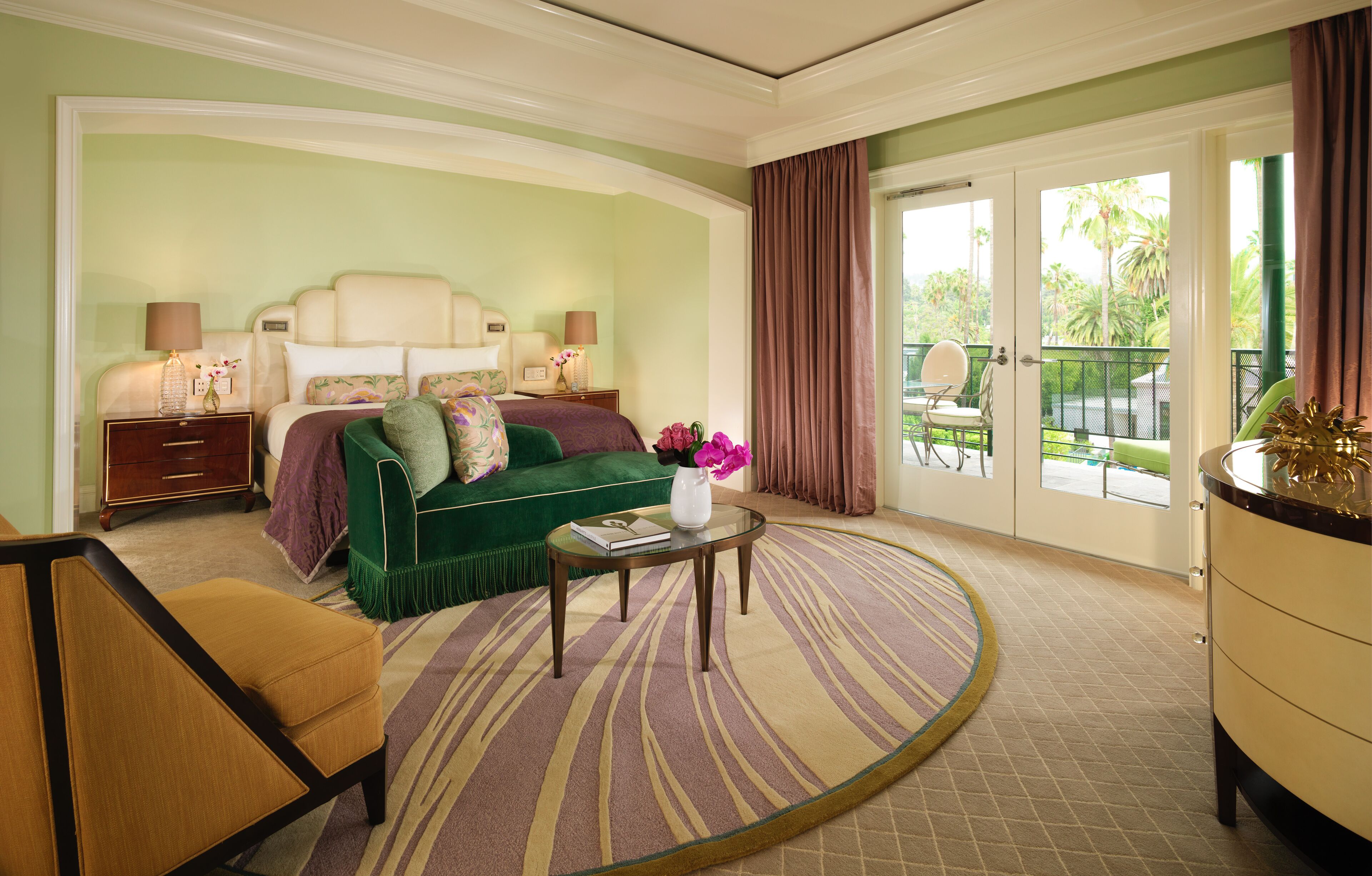 Ein Hotelzimmer mit Bett, einem grünen Sofa, einem kleinen Tisch mit einer Vase und Blick ins Freie.