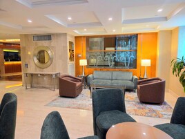A hotel lobby with a reception desk, seating area with sofas and armchairs, a coffee table, and a large mirror.