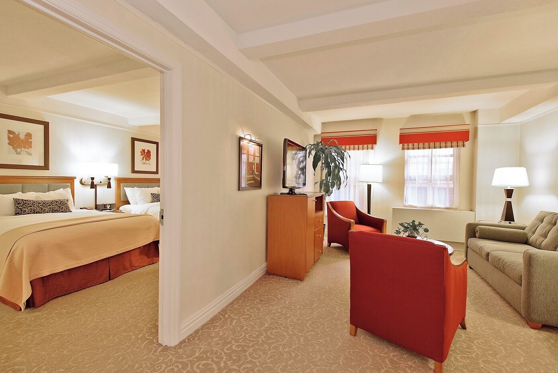 A hotel room with a bed, a red armchair, a sofa, a wooden cabinet, and a television.