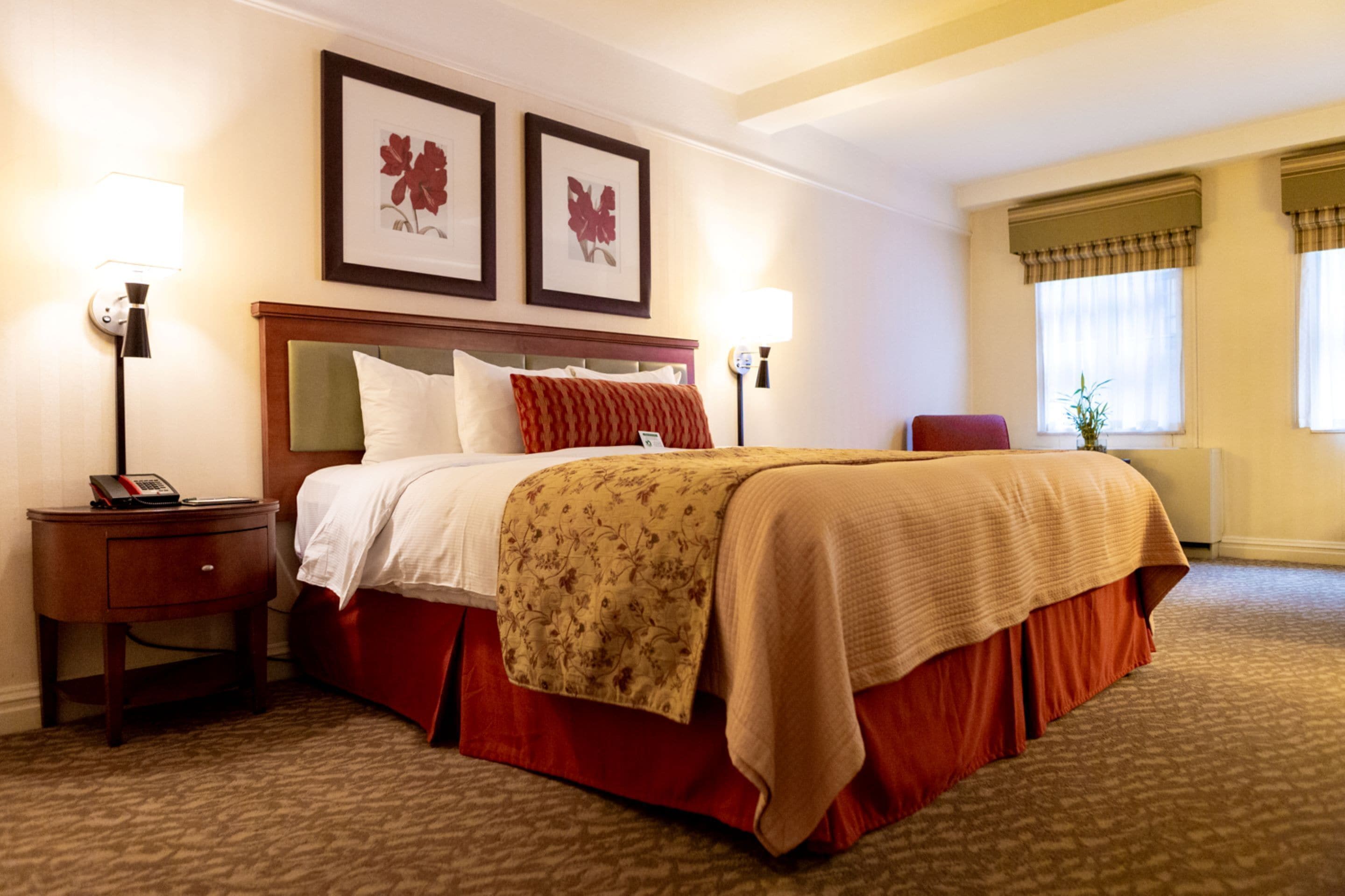 Habitación de hotel con una cama grande, dos lámparas de noche, una mesita de noche con un teléfono y una obra de arte floral enmarcada en la pared.