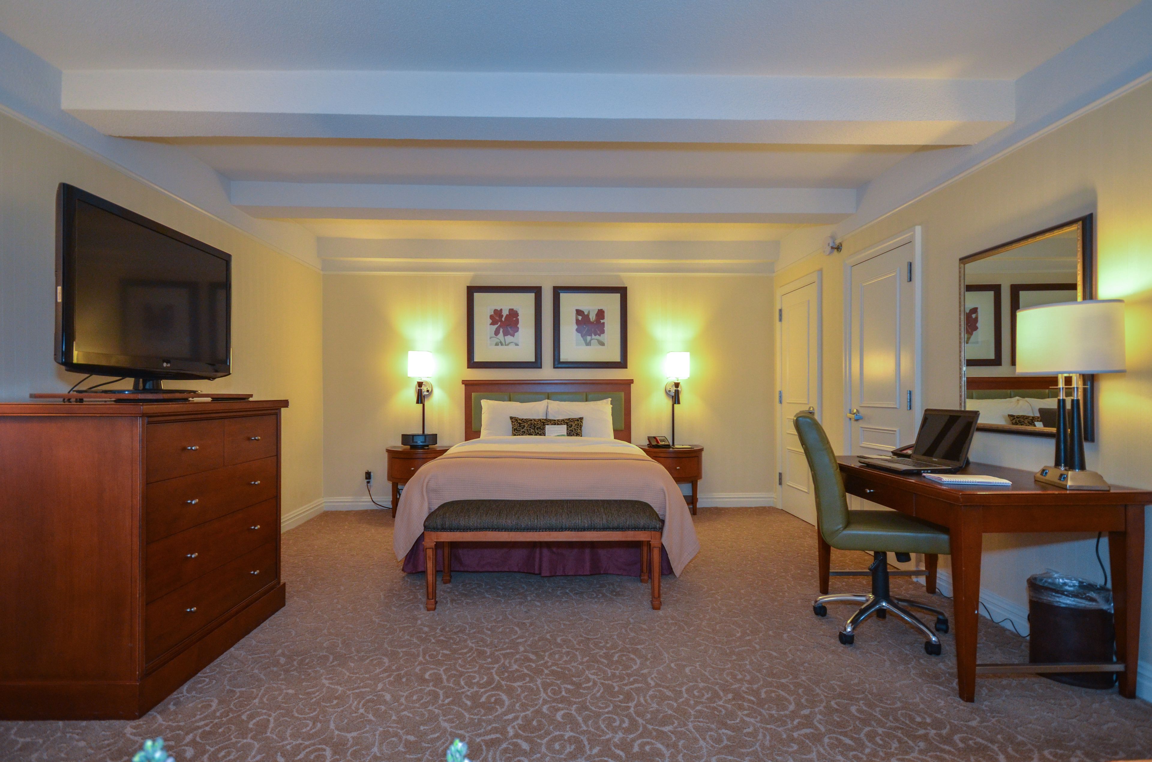 A hotel room with a bed, a desk with a computer, a TV, and two bedside lamps.