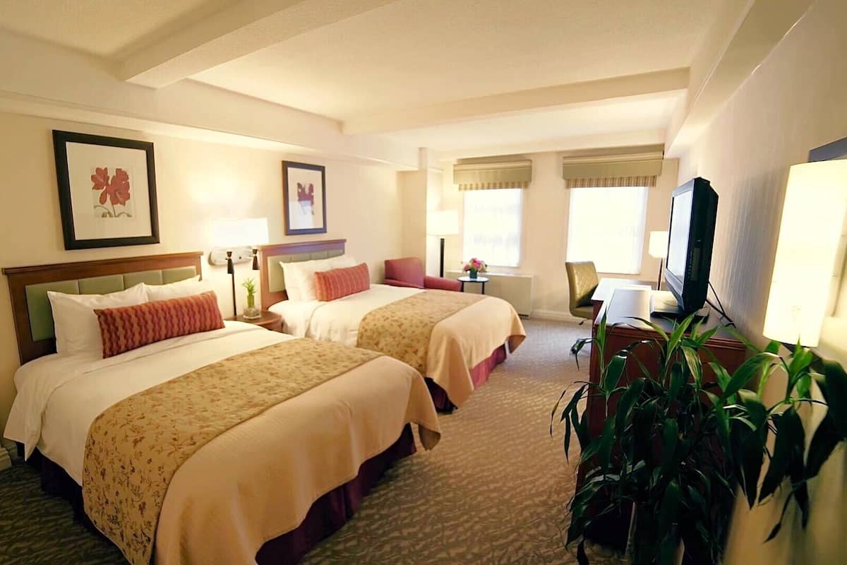 A hotel room with two beds, a television, a desk, and a potted plant.