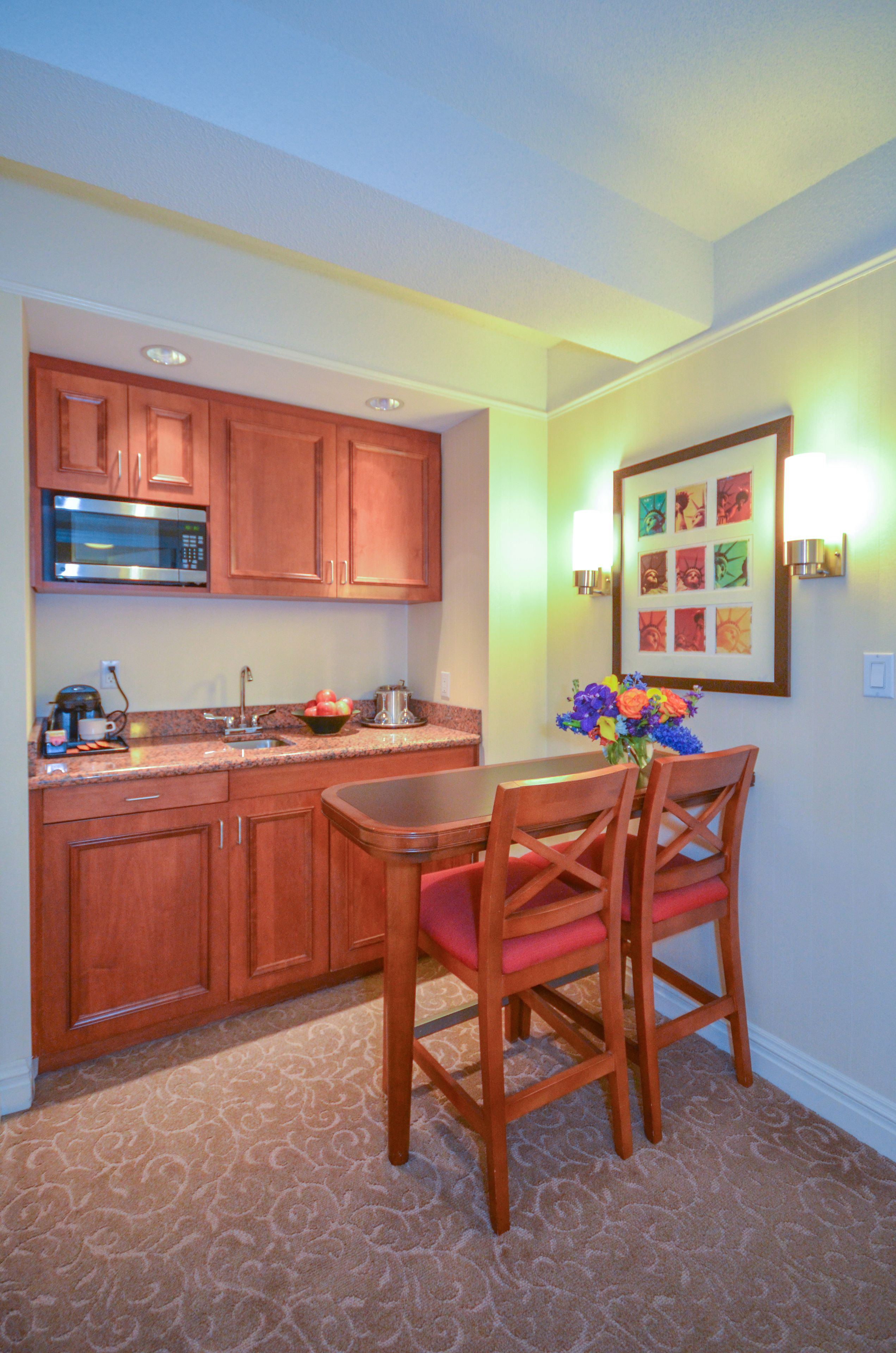 A kitchen with wooden cabinets, a microwave, a sink, and a dining area with a table and chairs.