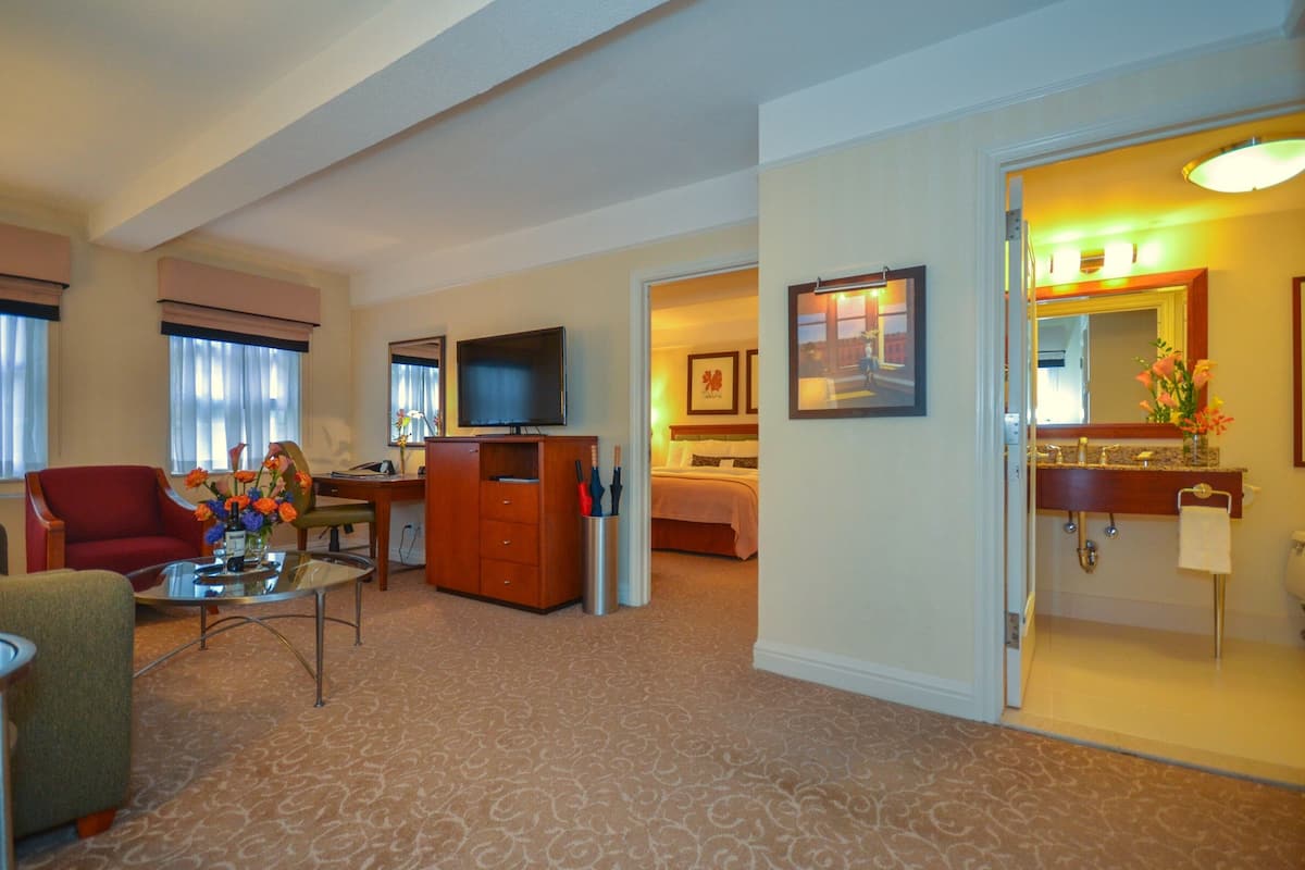A hotel room with a living area, a TV, a bed, a bathroom with a mirror, and a door leading to another room.