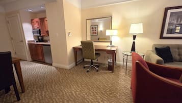 Habitación de hotel con kitchenette, escritorio con silla, una pequeña mesa redonda, sofá y lámpara.