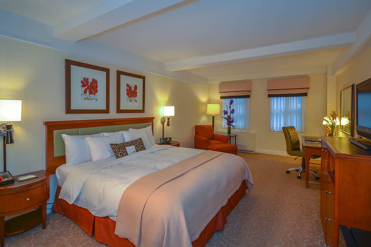A hotel room with a large bed, two bedside tables, a desk with a chair, a television, and framed artwork on the wall.