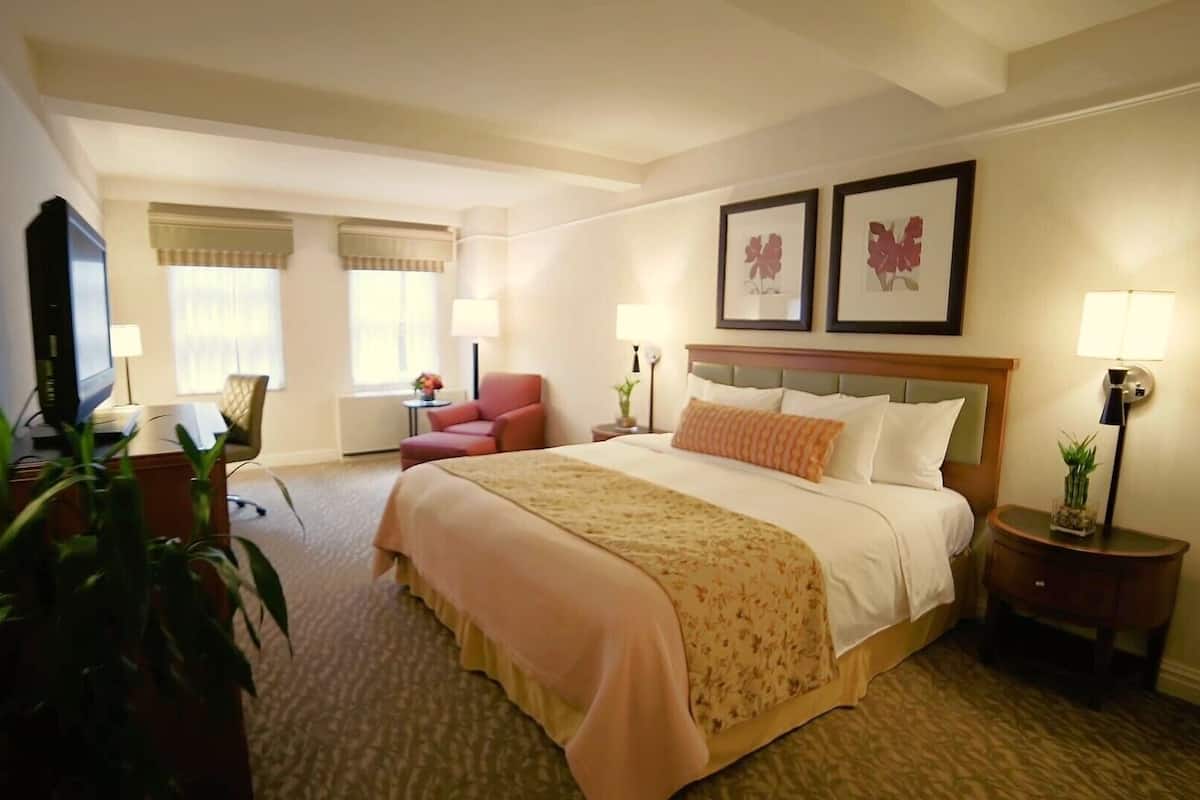 A hotel room with a large bed, a desk with a chair, a television, and two framed pictures on the wall.