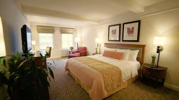 A hotel room with a large bed, a desk with a chair, a television, and two framed pictures on the wall.