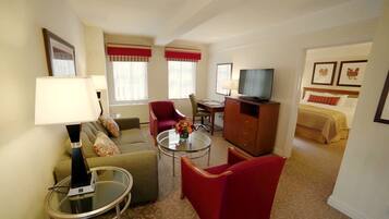 Hotelkamer met een bank, fauteuil, salontafel, televisie, bureau en een bed met een rode hoofdbord.