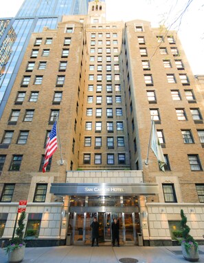 A hotel entrance with a classic brick facade, large windows, and an American flag. - San Carlos Hotel (New York)