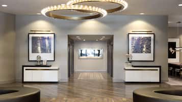 Um saguão de hotel com design moderno, apresentando um corredor central, dois balcões de recepção e uma luminária circular única.