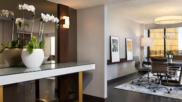 A modern office space with a glass table, potted orchids, a conference table with chairs, and framed artwork on the wall.