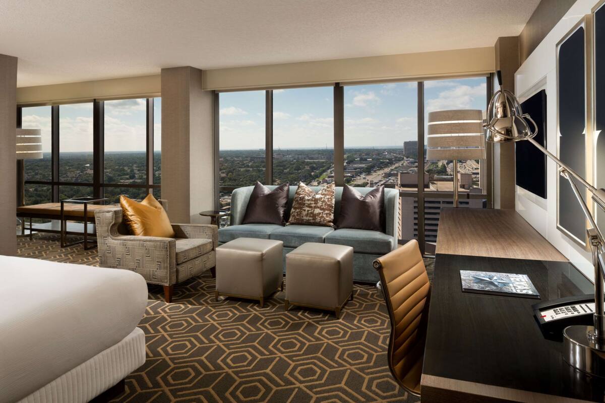 A hotel room with a large window, a sofa, a chair, a desk, and a bed.