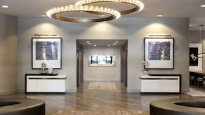 Een moderne lobby met een centrale doorgang, twee zijtafels en een rond hanglamp erboven.