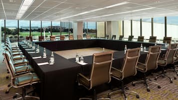 Un salón de conferencias con una mesa larga, sillas y botellas de agua.