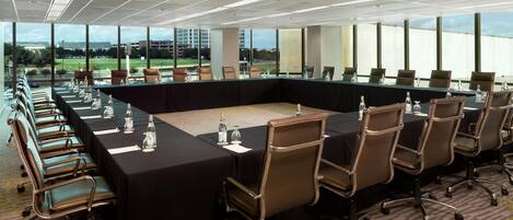 Un salón de conferencias con una mesa larga, sillas y botellas de agua.