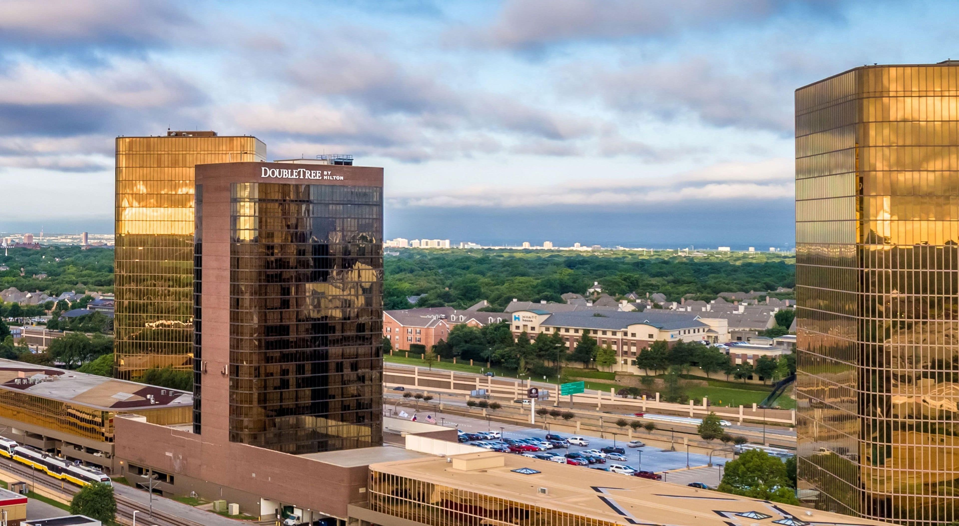 A modern building with a glass facade, a parking lot, and a highway in the background.