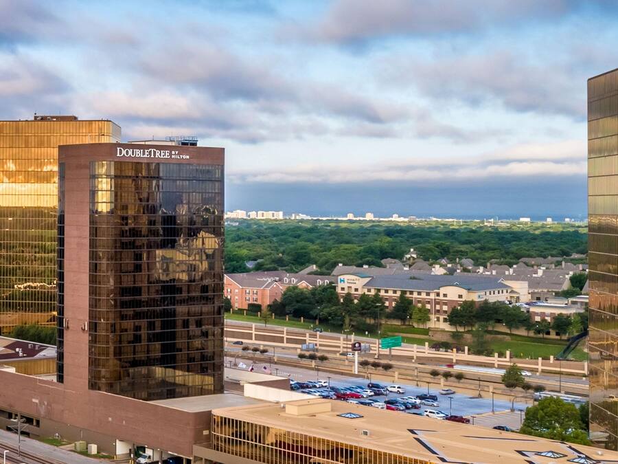 A modern building with a glass facade, a parking lot, and a highway in the background.