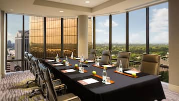 A conference room with a long table, chairs, water bottles, and a view of a cityscape through large windows.