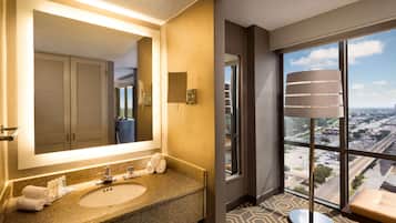 A hotel bathroom with a large mirror, a sink, and a window offering a city view.